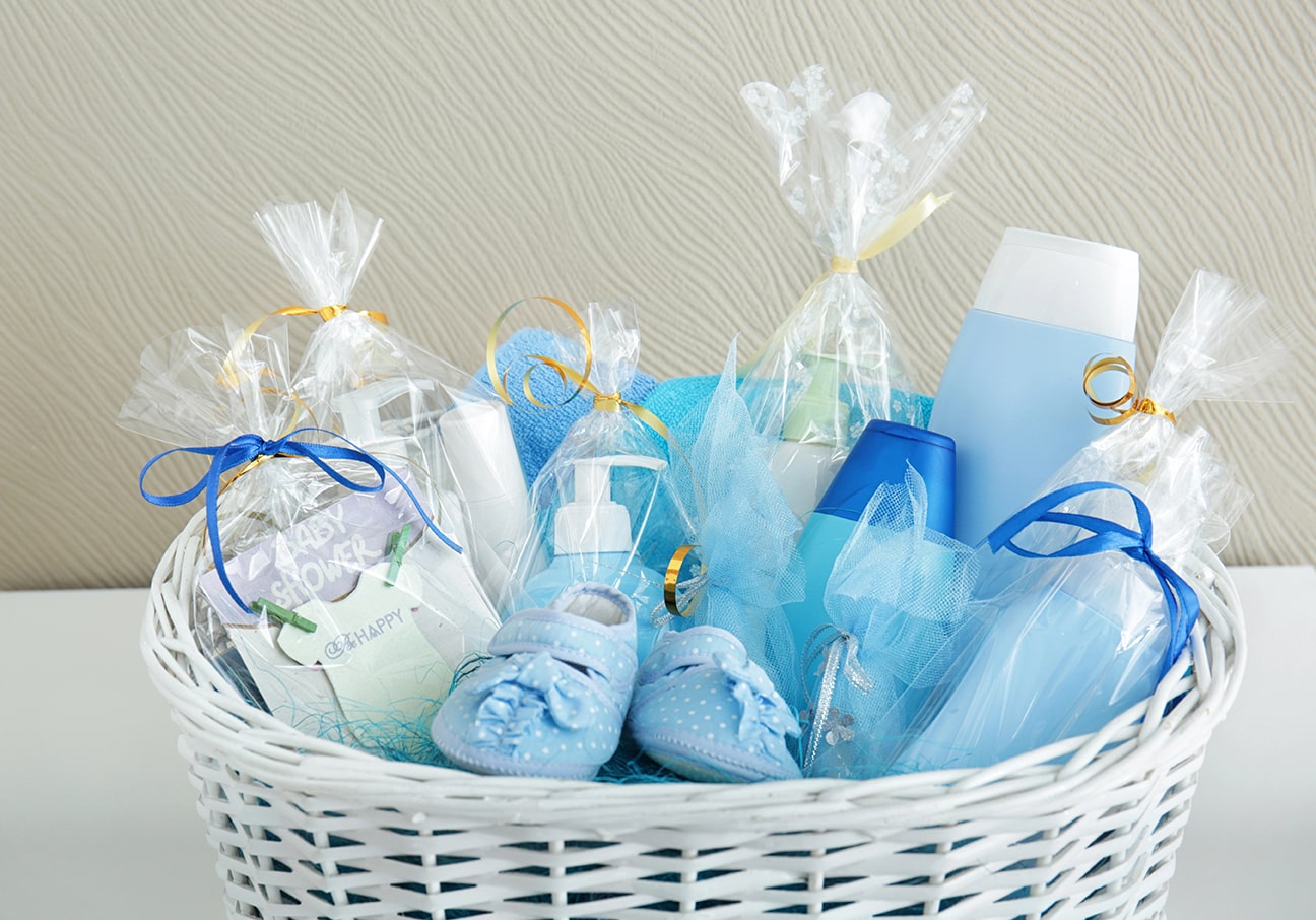 Witte mand met babyshowercadeaus in blauw thema, gevuld met verzorgingsproducten, slofjes en linten – inspiratie voor cadeau-ideeën.