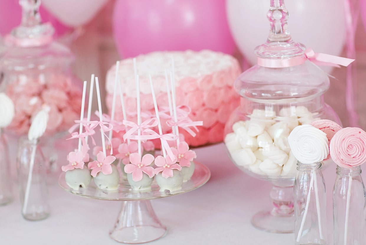 Zoete tafel in roze babyshowerstijl met cakepops, taart en glazen potten met snoep – feestelijke decoratie en hapjes.