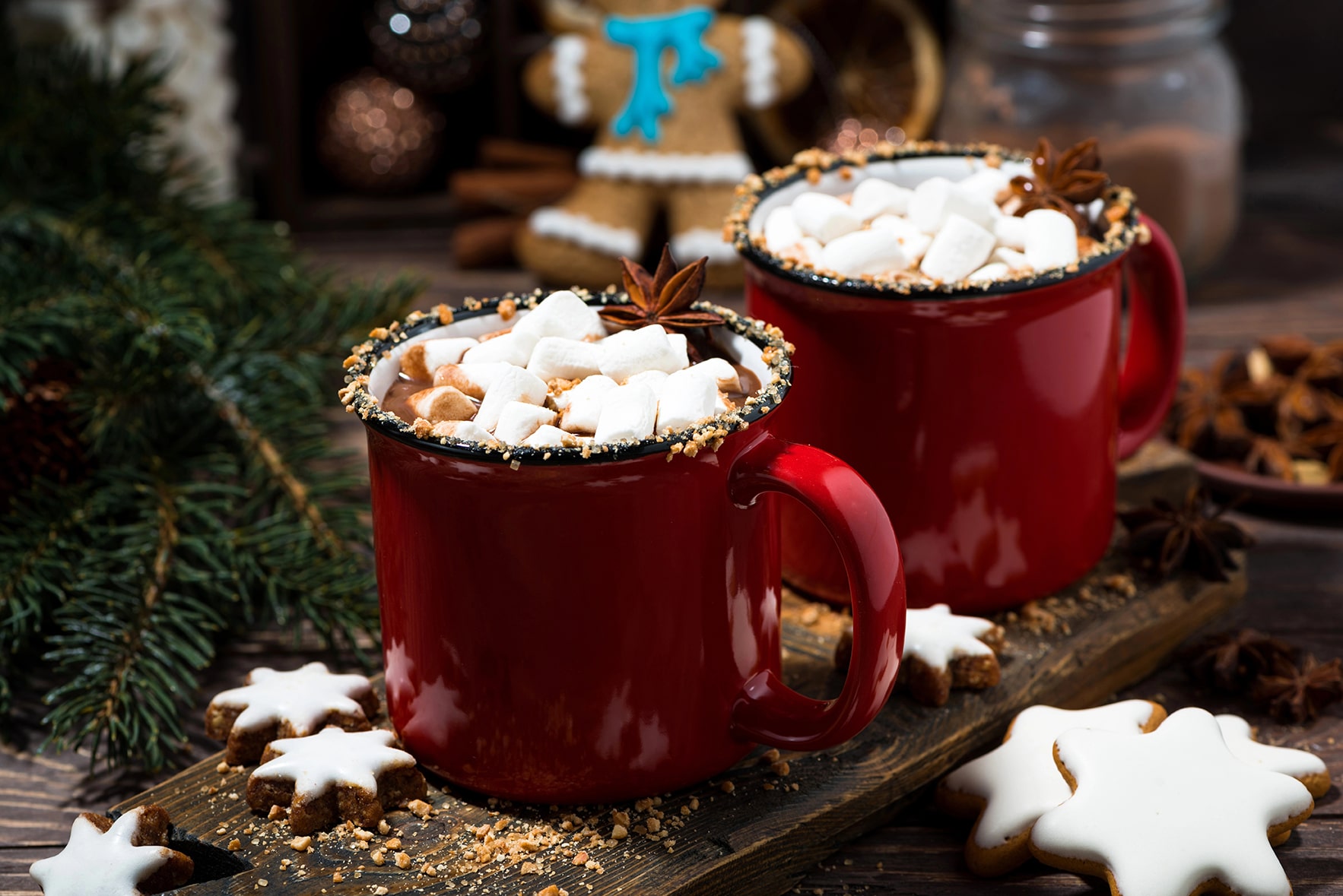 Twee rode mokken warme chocolademelk met marshmallows, kaneel en steranijs op een houten tafel – cosy winter babyshower sfeer.
